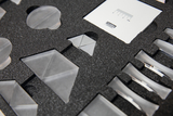 The image shows an arrangement of transparent geometric shapes placed in a textured foam insert. These materials can be used for experimental purposes in education to illustrate physics concepts.