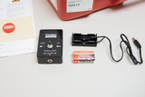 The picture shows experiment material for teaching, including a device for controlling a laser and an LED. Next to it is a battery compartment and two batteries that are needed to operate the device.