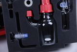 The image shows various laboratory instruments, including a glass jar with a red cap and other transparent supplies arranged in a padded foam insert. These materials are likely part of an educational experiment kit.