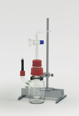 The picture shows a chemical experiment device consisting of a glass vessel with red screw caps and various glass tubes. It is mounted on a stable stand and is used for conducting experiments in the educational field.