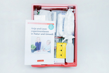 The picture shows a red box with experiment materials for kindergarten, which contains various utensils such as bottles, sprayers and sealed containers. On top is a book entitled &quot;Anja and Leon experiment in nature and the environment&quot;, which provides instructions.