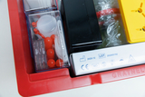 The image shows a red container with various experimental materials, including containers for small parts, red balls, and various tool parts. Safety and manufacturing information is also visible on the container.
