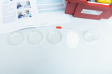 The image shows materials for an experiment, including several Petri dishes, a pipette, and a measuring cup. An open manual is also visible, containing instructions for conducting the experiment.