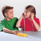The picture shows two children working together on an experiment. The girl is wearing earphones and holding a tube connected to a yellow device, while the boy is actively working on the device.