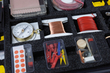 The picture shows a set of experiment materials that includes a compass, spools of wire in different colors, and various small containers of accessories. These items are arranged in a textured foam setup that allows for organized access.