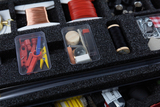 The picture shows a clear assortment of experimental materials in a foam box, including colored plastic parts, wooden parts and other crafting utensils. These materials are intended for educational purposes in the German school system.