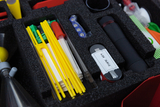 The picture shows a collection of experimental materials in a padded case. Various instruments and accessories, including yellow rods, containers and a flashlight, can be seen that can be used for scientific experiments.