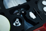 The image shows a collection of experimental materials arranged in a padded case. Visible items include measuring cups, a pipette, chemicals and safety goggles used for teaching science.