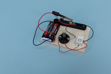The picture shows a simple circuit consisting of two batteries, a lamp and a switch mounted on a wooden board. This construction is probably intended for conducting experiments in educational settings to teach the basics of electricity.