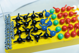 The picture shows a set of plastic model building caps in different colors that can be used as building blocks for chemical structures. There are black, red, green, blue and white pieces arranged on a yellow tray.