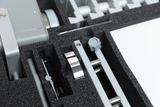 The picture shows various metallic and grey components neatly arranged in a padded foam tray. These parts appear to belong to an experimental device designed for educational purposes in the German school system.