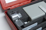 The picture shows a red suitcase lined with foam and containing various experimental materials. Among other things, a gray device as well as two small glasses and a mirror are visible, which can be used for educational purposes.