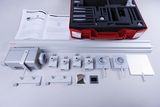 The picture shows an experiment kit with various optical devices and accessories arranged in a red storage box. In addition to a textbook with instructions, you can see elements such as lenses, mirrors and holders that can be used for scientific experiments.