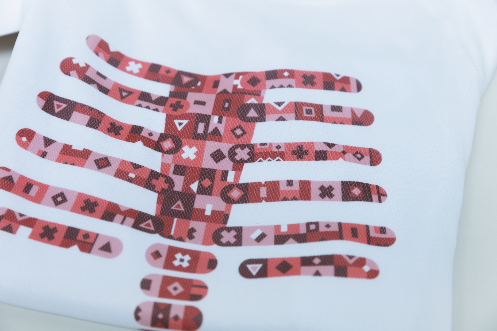 The image shows a T-shirt with a creative print in the shape of a hand. The illustration consists of various geometric patterns in shades of red, which stand out on a white background.