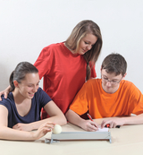 The picture shows three people working on an experiment. One person has a ball on a sled while another takes notes and observes and assists the third person.