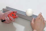 The picture shows a handheld stopwatch in one hand and a white ball positioned on a rail. This arrangement is probably used for physics experiments to measure movement or time.