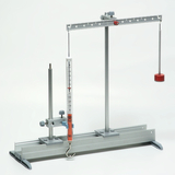 The picture shows a physical experimental setup with a hanging pendulum and a measuring scale. The apparatus is used to conduct experiments to investigate forces and movements.