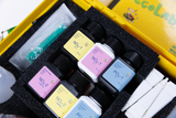 The picture shows an experiment kit with various chemicals in small bottles encased in foam. The labels on the bottles identify different chemical substances that can be used for educational experiments.