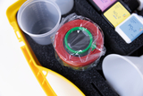 The picture shows an experiment case with various laboratory equipment and chemicals. You can see transparent beakers, a red-green device and several vials with different color codes that are used for scientific experiments.