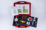 The picture shows a red suitcase filled with experimental materials for school purposes. Next to a manual, various scientific devices and tools such as sample containers, measuring instruments and experimental setups are arranged.