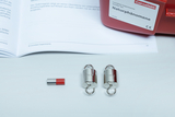 The picture shows an experiment set consisting of two 50 g weights and a small magnet. In the background you can see an open book with information about natural phenomena, which is part of the set.