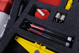 The picture shows a selection of experimental materials neatly arranged in a foam tray. These include two transparent test tubes with a red liquid, a red object and various other devices and utensils.
