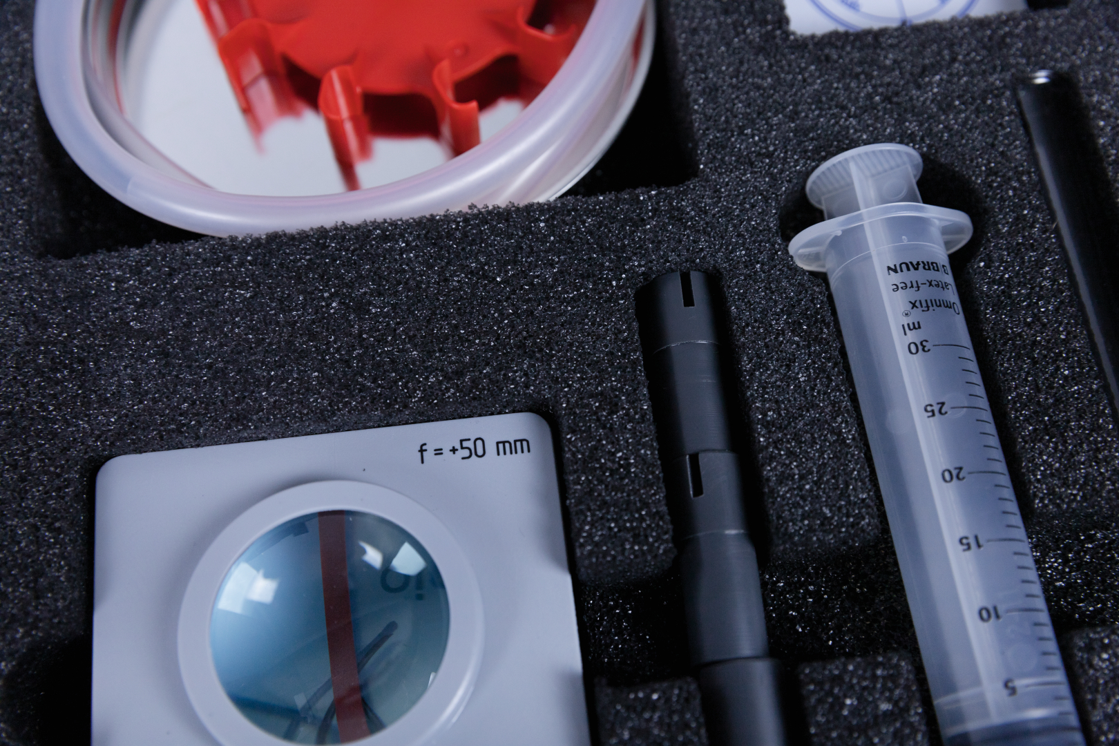 The image shows various experimental equipment arranged in a padded case. The items include a lens, a syringe and other components that can be used for scientific experiments in educational settings.