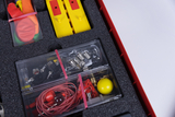 The picture shows a box with experimental materials that are suitable for teaching in the German education system. The box contains various objects such as balloons, small electrical components and metal components that can be used for various experiments.