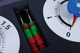 The picture shows a set of experimental materials consisting of colored building blocks and a measuring device. The building blocks are red and green and are located in a recess, while the measuring device is clearly calibrated.