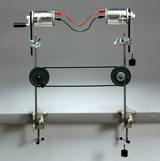 The picture shows an experimental device with two electric motors connected to each other via belts and pulleys. It is used to illustrate physical principles such as energy transfer and the mechanics of movement.