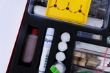 The image shows an experiment kit with various materials and equipment, including bottles, chemicals and containers, arranged in a padded compartment. It is designed to enable students to conduct hands-on experiments and make scientific discoveries.