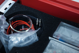 The picture shows an experiment kit containing various items including a glass jar and red wires. The items are neatly arranged in a padded box for use in educational experiments.
