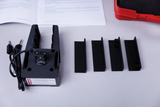 The picture shows an experimental device with a base and several black brackets lying next to it. Next to the device is a manual that contains instructions on how to use it.
