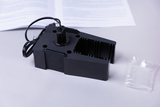 The picture shows a black experimental device with a connector and a chamber that appears to be used for scientific purposes. Next to the device is a small bag and an opened manual that provides further information.