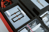 The picture shows an experiment station housed in a foam insert of a suitcase. It shows a circuit board with connections, white components and cables used for scientific experiments in the educational field.