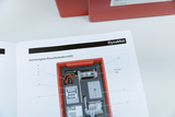 The picture shows a manual for an experimental device called DynaMot, which provides detailed information about the individual parts included. The picture shows various components such as the motor and line reel in a red housing.