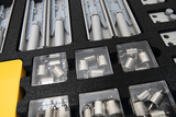 The picture shows a sorted box with experimental materials that can be used for various physics experiments. The box contains weights in transparent compartments as well as various holders and components.