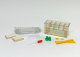 The picture shows a set of experimental supplies consisting of a transparent container with compartments, two stacks of small, light-colored plates, a pipette, green building blocks, yellow rods and some small holders. It is suitable for educational purposes for conducting experiments.