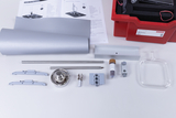 The picture shows a collection of experimental materials arranged on a table, including a red suitcase, various metal and plastic parts, a glass container and instructions. These materials are presumably intended for conducting thermodynamics experiments in educational settings.