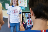 The picture shows a child wearing a special T-shirt with an anatomical design while another child takes a photo of it with a tablet. On the tablet&#39;s screen, additional anatomical information such as &quot;back muscles&quot; is visible.