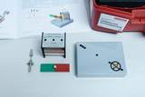 The picture shows various experimental materials for demonstrating induction and alternating current, including a coil, a magnet and a control unit. Alongside these materials is a manual containing explanatory diagrams and information.