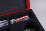 The picture shows a padded foam insert of an experimental cage in which various scientific materials are stored. You can see a red tube, small objects in a transparent cover and a metal tool.
