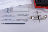 The image shows an arrangement of experimental materials, including brackets, chains and a weighing mechanism. Additionally, a manual and a red toolbox-like element can be seen in the background, which are used for conducting experiments in educational settings.