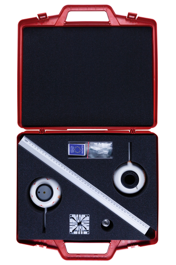 The picture shows an open red suitcase filled with educational experiment materials. Included are various sealed items, a ruler and optical devices arranged in foam storage.