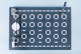 The image shows an experimental platform with a multitude of round holes in a grid pattern that can be used for wiring. On the top you can see connectors for plus and minus polarities to create circuits.