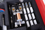 The picture shows an experiment kit that includes a coil, various electrical components, and several white objects, presumably magnets or switches. The contents are neatly arranged in a foam insert that provides protection and keeps the parts in place.