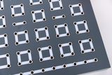 The picture shows a flat, gray plate with multiple arrangements of silver vias and white, rectangular conductor tracks. This is probably used for experimental electronic applications in the educational sector.