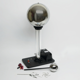The picture shows an electrostatic device, such as a Van de Graaff generator, with a large metal ball on a stable base. Next to the device are various accessories that can be used for educational experiments.