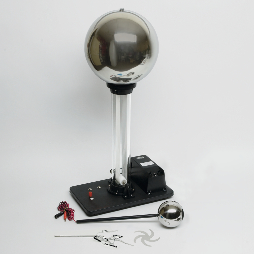 The picture shows an electrostatic device, such as a Van de Graaff generator, with a large metal ball on a stable base. Next to the device are various accessories that can be used for educational experiments.