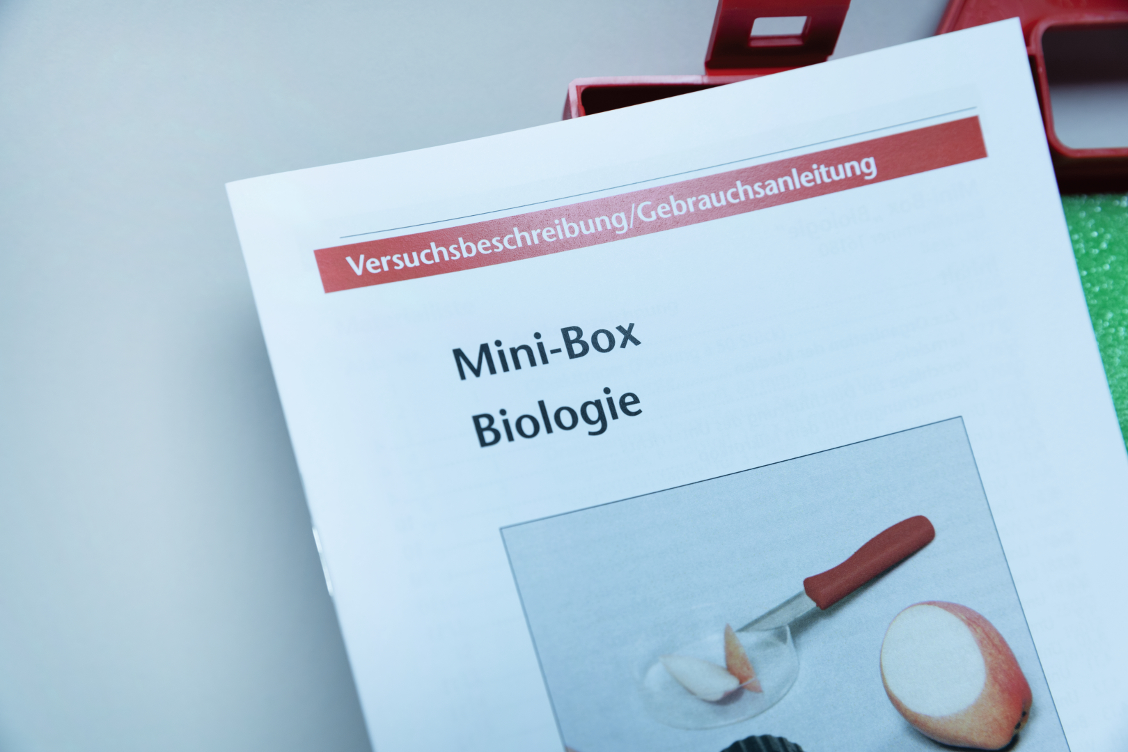 The picture shows the instruction manual for a mini box for biological experiment supplies in the German education system. The instructions show a picture of a meal being prepared using a knife and an apple.